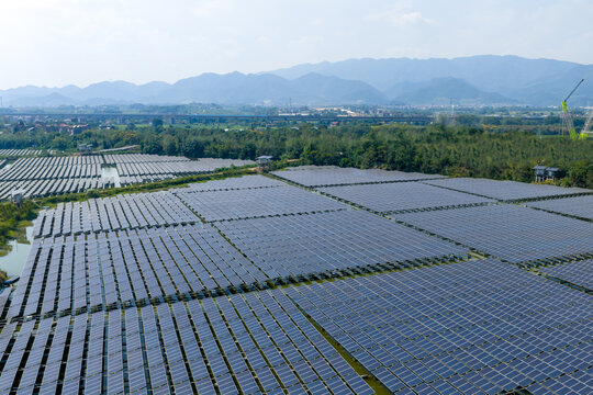 Aerial view of large-scale photovoltaic power station array nestled among mountains and fields