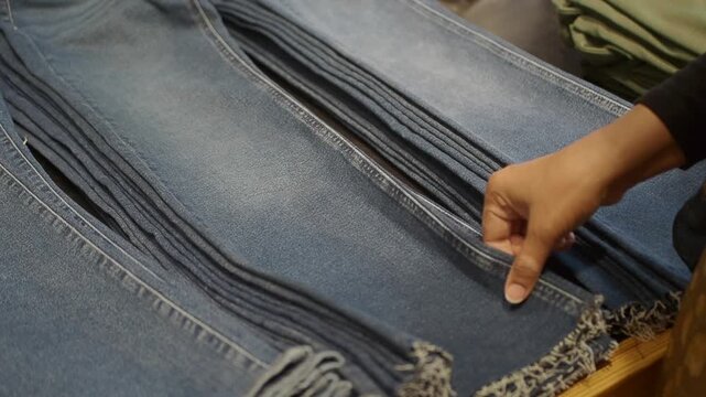 A woman is looking through a stack of folded jeans in a store