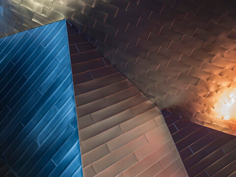 Close-up of angular metal panel cladding on a building exterior, where multiple faceted surfaces meet at sharp diagonal edges. 