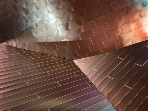 Close-up of angular metal panel cladding on a building exterior, where three distinct planes meet at sharp diagonal ridges. 