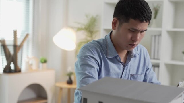 Focused Asian Architect Using Calculator and Writing Notes on Blueprint in Office