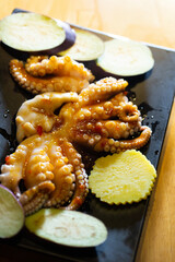 Fresh raw baby octopus marinated in savory soy sauce with sliced eggplant and zucchini on a black plate © mnimage