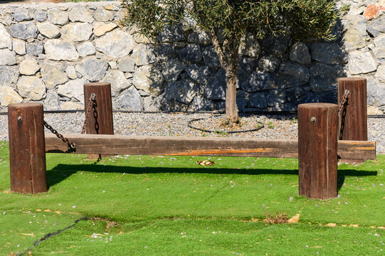 A rustic balancing beam made of wood and chains in a sunlit park surrounded by stone walls and grass