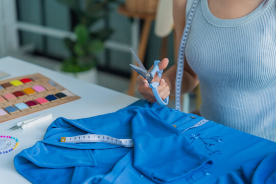 Asian woman tailor using scissors to cut off excess threads.