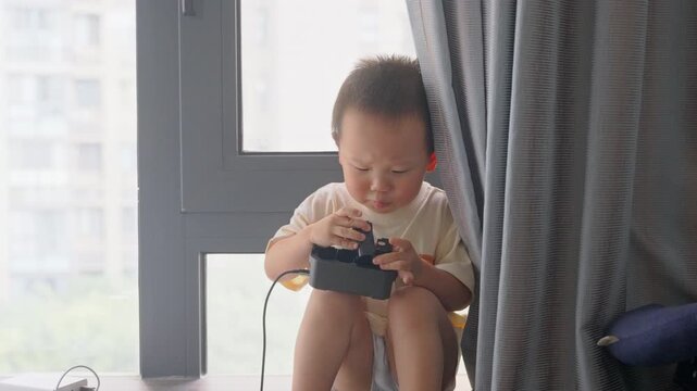 Half-length view of toddler playing with charging adapter by window