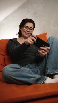 Woman sits on a couch in a relaxed living room while looking at her phone