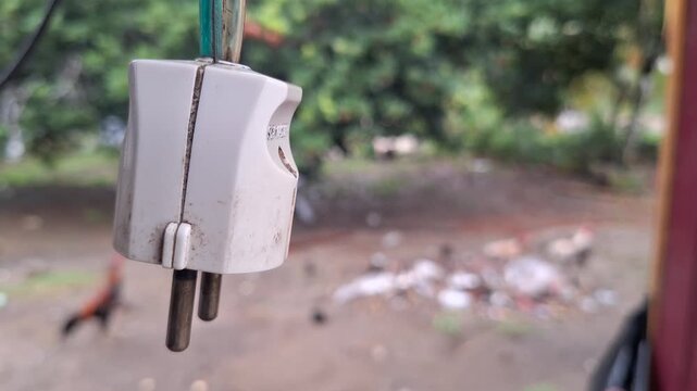 Close up of a white electric plug hanging with blurred outdoor background during day time
