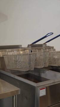 Clean stainless steel commercial deep fryer with empty wire baskets in a professional restaurant kitchen, modern food service equipment.