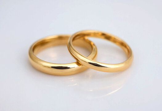 Two golden wedding rings placed closely together on white surface