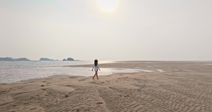 Young woman walking vast sandy beach at low tide, contemplating the ocean and distant tropical islands under bright sky, conveying sense of freedom and serenity. Travel and explore Ko Lanta, Thailand