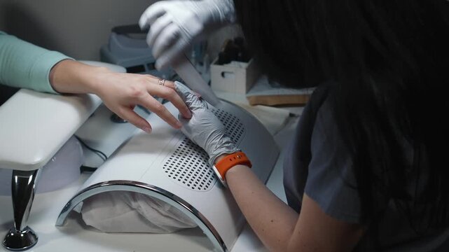 Manicure technician files nail with hand file in beauty salon during professional hand care procedure