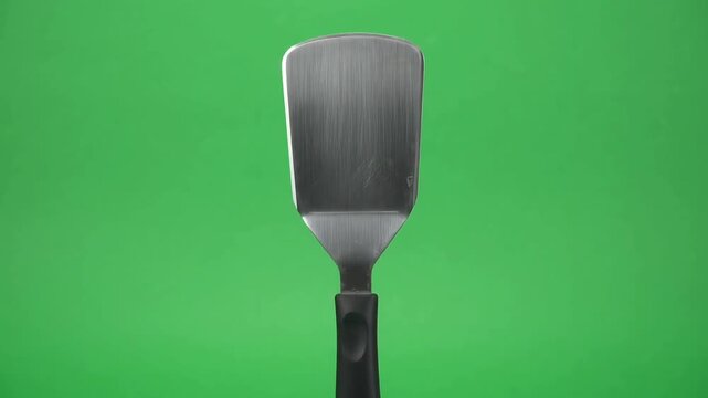 Stainless steel spatula rotating against a green screen background