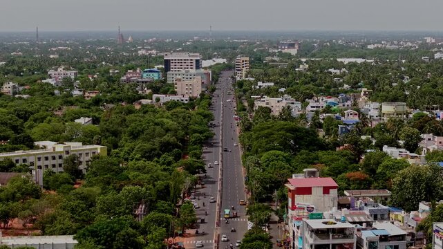Aerial drone view shows the highway and surrounding urban landscape leading toward Brihadeeswara Temple. Buildings trees and roads extend across Thanjavur Tamil Nadu