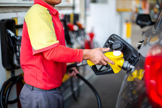 Worker refilling petrol to a black car using a yellow fuel nozzle nozzle at a gas station. Concept of energy, transportation, and automotive service.