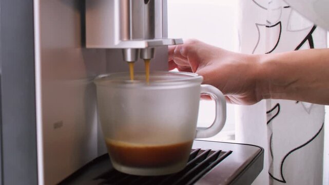 Espresso brewing. Drink preparing. Female hands using automatic coffee machine for fresh morning beverage at home kitchen indoor.