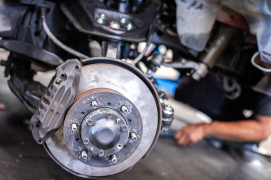 Detailed view of a car disc brake system and suspension with blurry mechanic working in the background. Concept of auto repair, safety inspection, and vehicle maintenance.