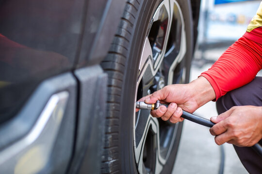 Close-up of a mechanic checking and inflating a car tire pressure using an air pressure gauge at a gas station for safety and vehicle maintenance.