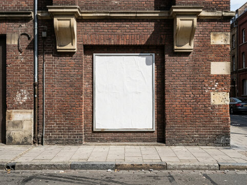 An empty blank promotional poster frame mounted on an aged red brick exterior wall in a European city street, creating a versatile placeholder for urban advertising campaigns and media displays