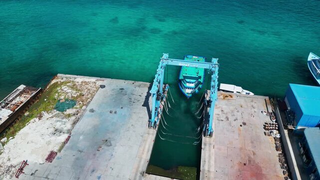 Drone shot of maritime boat hoist lifting a vessel in shipyard slipway next to clear turquoise sea. Great background for industrial and marine engineering promo.Maldives