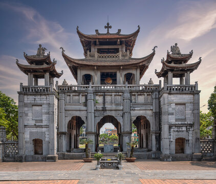 Historic stone bell tower gate of Phat Diem Cathedral in Ninh Binh, Vietnam, featuring a unique blend of Gothic architecture and traditional Vietnamese pagoda style under a sunset sky