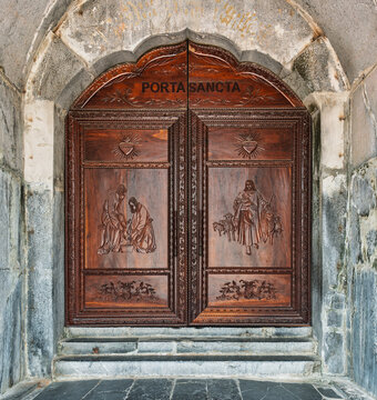 Detailed view of the intricately carved Porta Sancta wooden doors at the historic Phat Diem Cathedral in Ninh Binh, Vietnam, showcasing religious iconography set in a stone archway