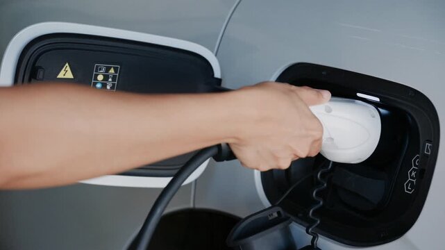 Person plugging in EV charging cable to white electric vehicle for sustainable energy transport.	