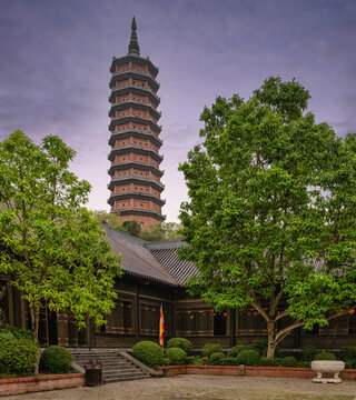 Bao Thien Tower at the Bai Dinh Pagoda complex in Ninh Binh, Vietnam, featuring traditional wooden architecture and lush greenery under a dramatic twilight sky