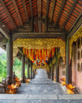 Covered walkway with intricate gold wood carvings and colorful prayer ribbons hanging over a stone staircase at Bai Dinh Pagoda in Ninh Binh, Vietnam
