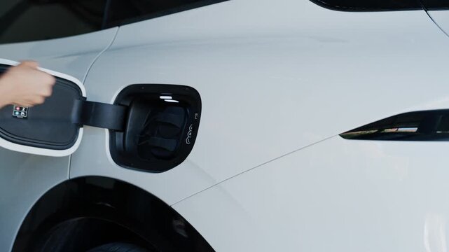 Person plugging in EV charging cable to white electric vehicle for sustainable energy transport.	