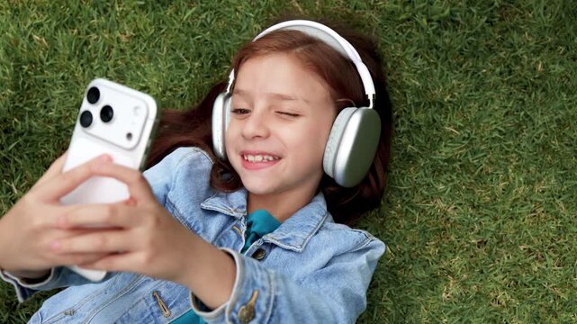 Happy redhead girl taking selfie photos with smartphone and headphones on grass - Technology, music and social media lifestyle concept