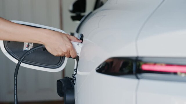 Person plugging off EV charging cable to white electric vehicle for sustainable energy transport.	
