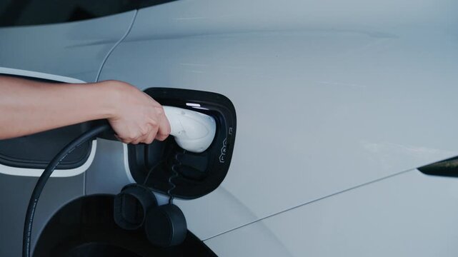 Person plugging off EV charging cable to white electric vehicle for sustainable energy transport.	