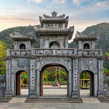 Ornate stone entrance gate of the Thai Vi Temple surrounded by scenic limestone karst mountains in Ninh Binh, Vietnam during golden hour