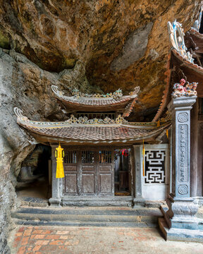 Traditional wooden shrine built into a rocky cave at Bich Dong Pagoda in Ninh Binh, Vietnam, featuring intricate roof details and ornate stone carvings