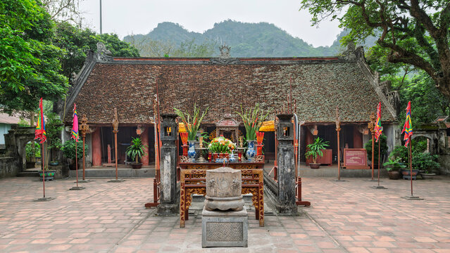Traditional architecture of the Temple of Emperor Le Dai Hanh at the Hoa Lu Ancient Capital in Ninh Binh, Vietnam, featuring a courtyard with a stone altar, incense burner and lush surroundings