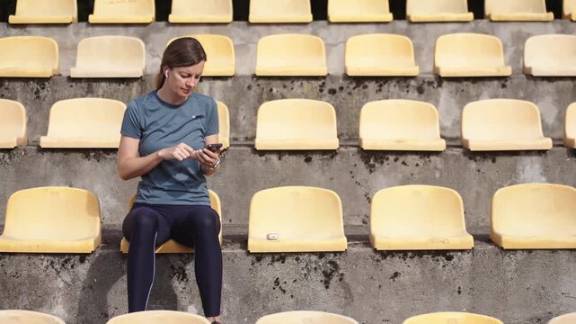 Woman using smartphone while sitting on stadium seats