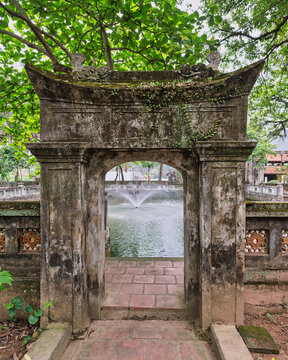 Ancient stone archway at the Temple of Emperor Le Dai Hanh in Hoa Lu Ancient Capital, Ninh Binh, Vietnam, featuring a tranquil garden pond with a fountain in the background