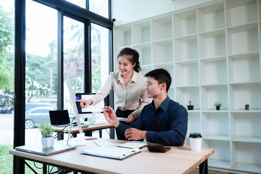 Asian business professionals collaborating on a creative project, discussing ideas and reviewing work on a computer in a modern office.