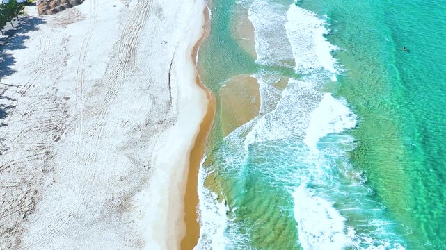Aerial top-down view of beautiful emerald ocean waves breaking on a white sand beach in South Korea.