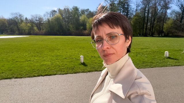 Horizontal POV photo of confident mature woman in glasses walking in sunny green park