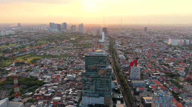 Aerial view of Surabaya, Indonesia at sunset, showing dense urban neighborhoods, modern high-rise buildings and city skyline in the warm evening light of East Java.