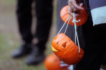 Fototapeta premium Carved Halloween Pumpkin Lanterns Handheld With White Ropes At Festival. Close-up of a person holding creative handmade jack-o-lantern buckets crafted from real pumpkins