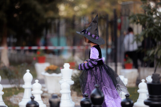 Little Girl In Witch Costume Holding Hands At Halloween Festival. Side view of a cute young girl wearing a black witch hat during an autumn celebration