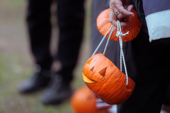 Carved Halloween Pumpkin Lanterns Handheld With White Ropes At Festival. Close-up of a person holding creative handmade jack-o-lantern buckets crafted from real pumpkins