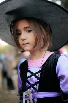 Portrait Of Cute Little Girl In Witch Costume At Halloween Autumn Festival. Close-up portrait of a thoughtful young girl wearing a black witch hat and festive dress
