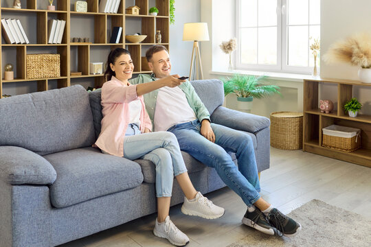 Couple relaxing on sofa with remote watching tv. They sit together in a cozy livingroom at home, enjoying streaming entertainment and modern comfort. Concept of leisure and connection.