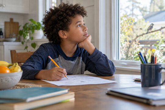 Child doing homework while distracted by a bird outside the window. ADHD and attention challenges concept. Childhood learning, focus and concentration. Education and home study