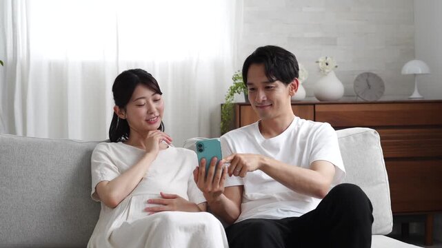 リビングでスマホを使う妊娠中の妻と夫