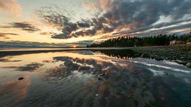 Time-lapse of sunset over a calm tidal beach with cloud reflections and evergreen forest edge in Pacific Northwest