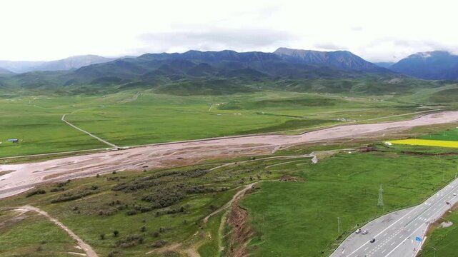 Aerial drone footage of Qilian Mountains grassland with winding river, highway, and rural settlements in Qinghai Province